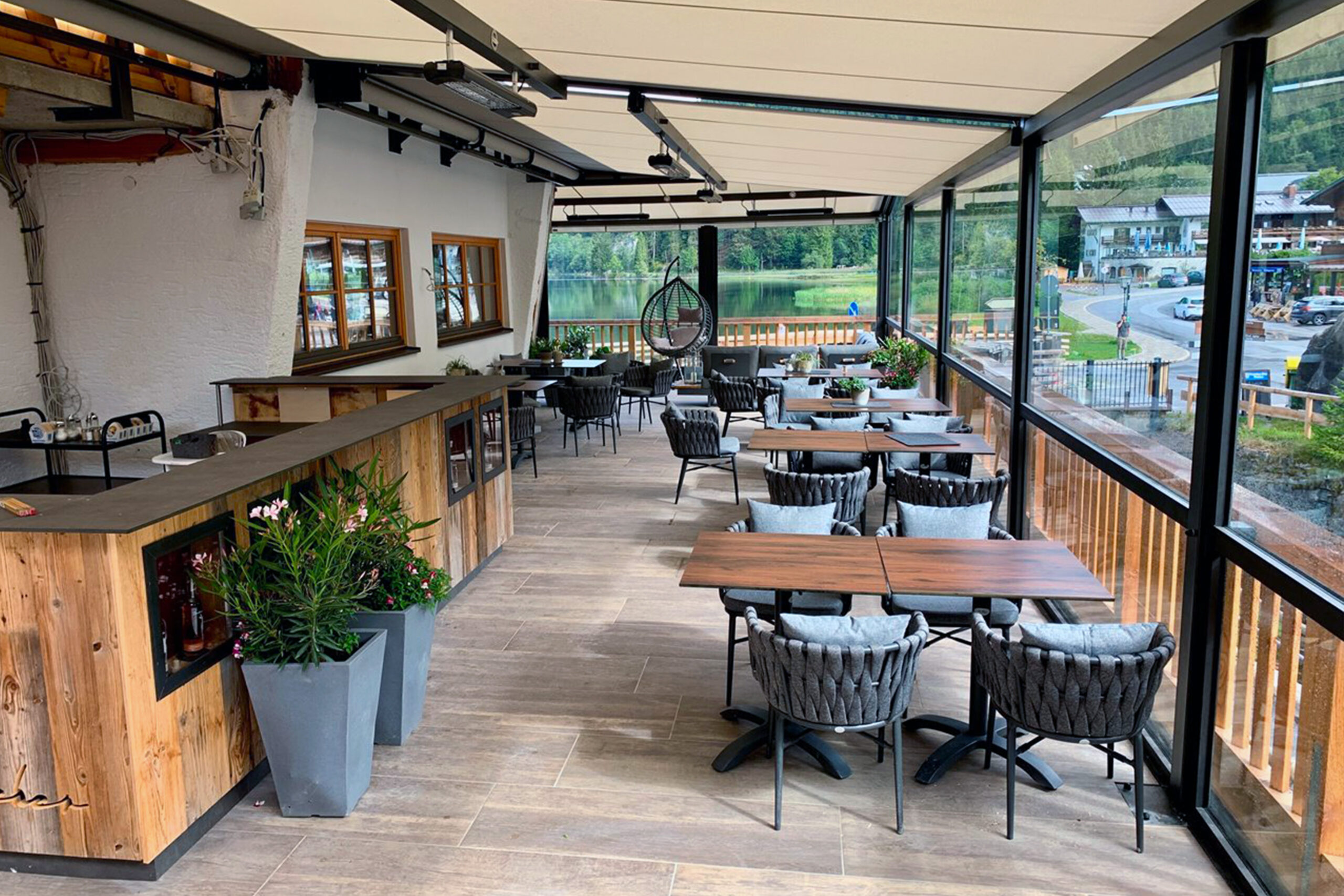 Restaurantterrasse mit integrierter Infrarot-Heizung unter einer modernen Glasüberdachung. Der stilvolle Gastronomiebereich mit Panoramablick auf See und Berglandschaft bietet Gästen ganzjährig angenehme Wärme und hohen Komfort im Außenbereich.