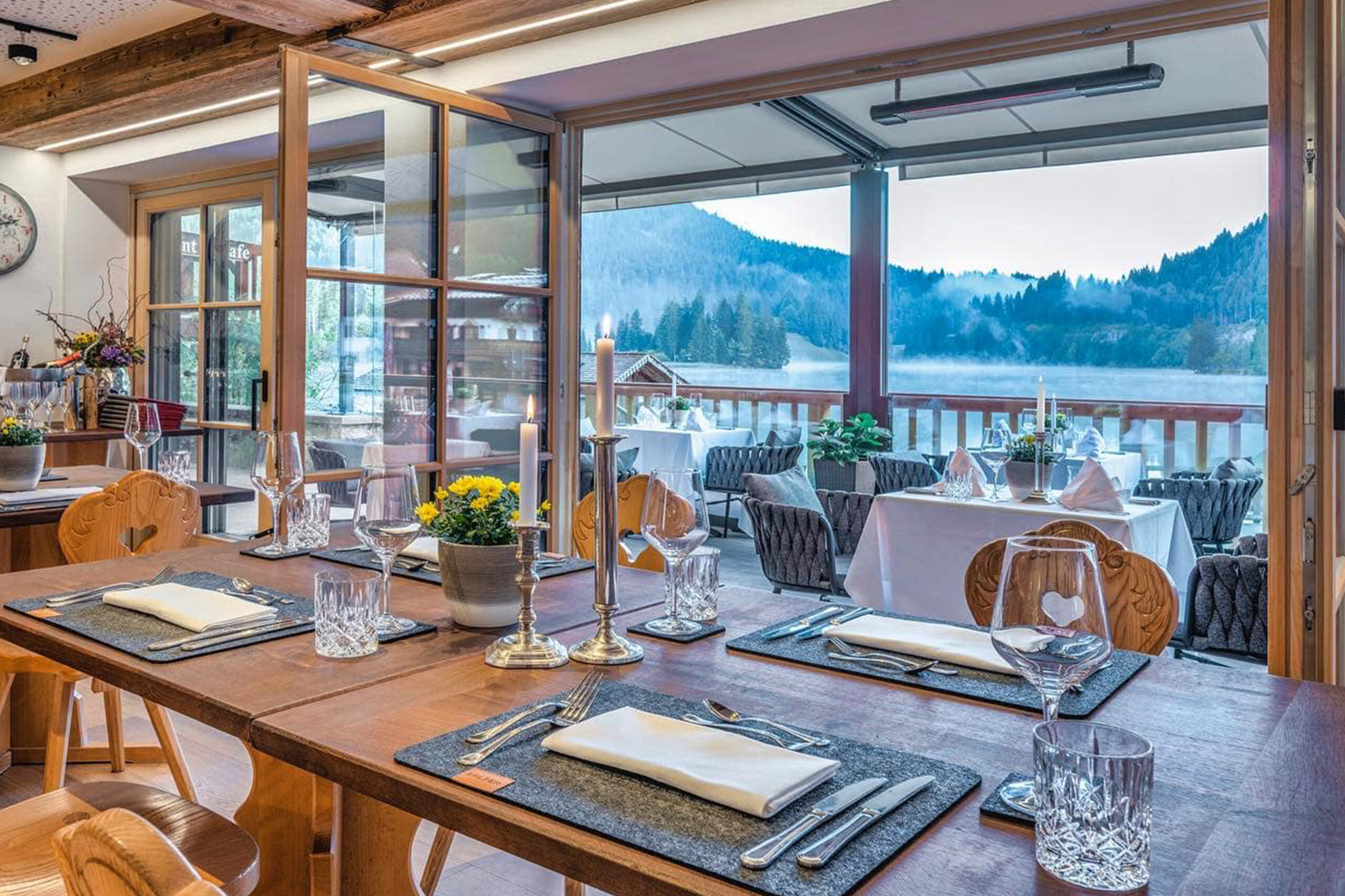 Restaurantterrasse mit integrierter Infrarot-Heizung unter einer modernen Glasüberdachung. Der stilvolle Gastronomiebereich mit Panoramablick auf See und Berglandschaft bietet Gästen ganzjährig angenehme Wärme und hohen Komfort im Außenbereich.