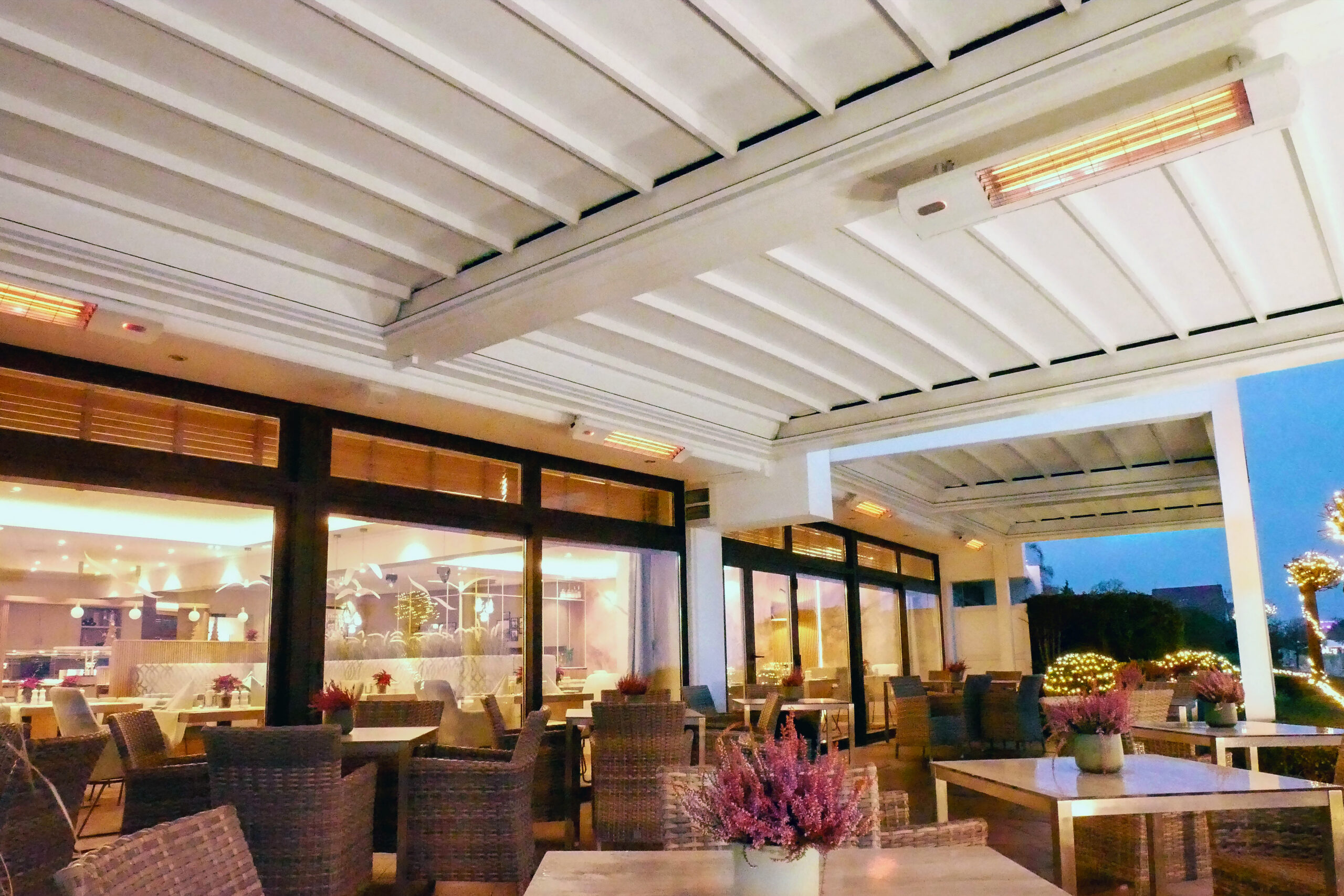 Restaurantterrasse mit integrierter Infrarot-Heizung unter einer modernen Glasüberdachung. Der stilvolle Gastronomiebereich mit Panoramablick auf See und Berglandschaft bietet Gästen ganzjährig angenehme Wärme und hohen Komfort im Außenbereich.