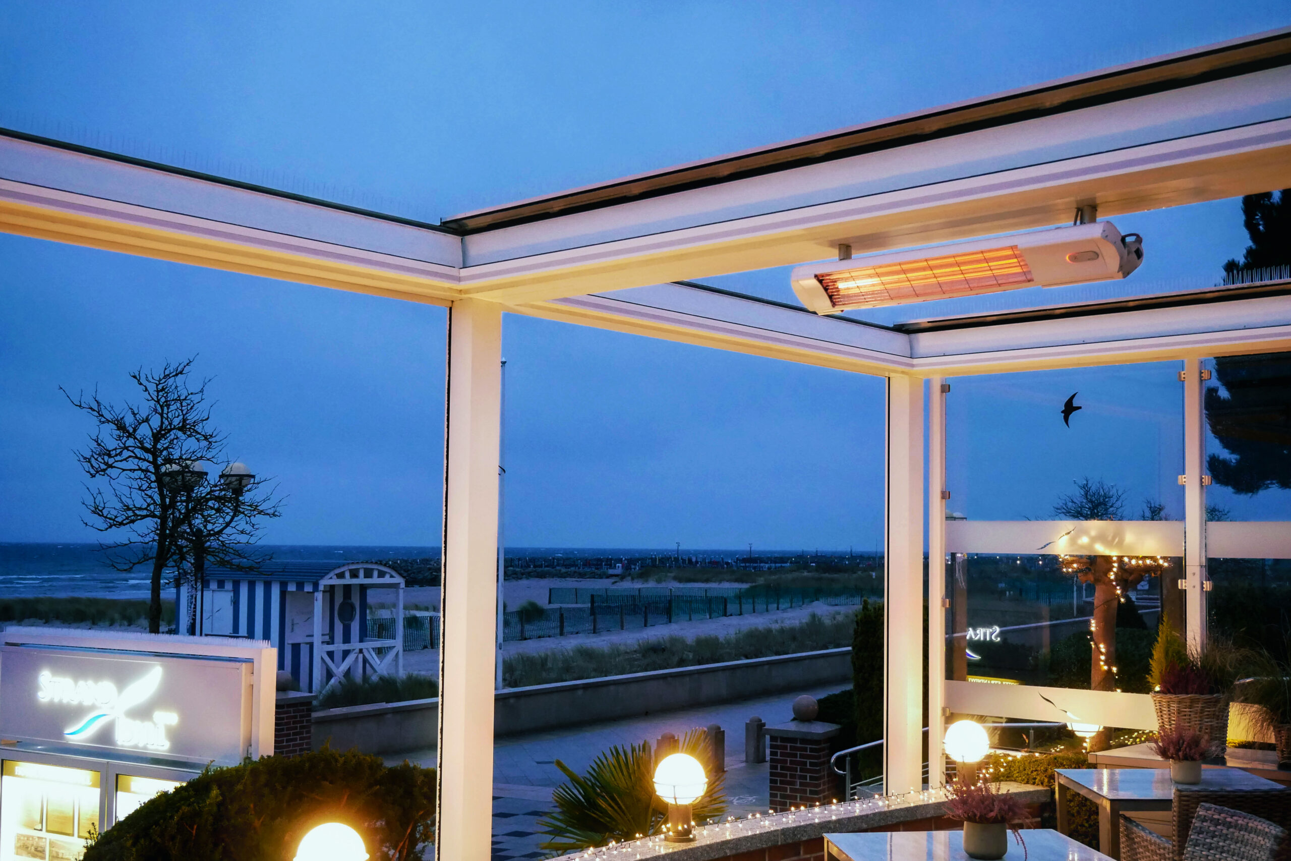 Restaurantterrasse mit integrierter Infrarot-Heizung unter einer modernen Glasüberdachung. Der stilvolle Gastronomiebereich mit Panoramablick auf die Ostsee bietet Gästen ganzjährig angenehme Wärme und hohen Komfort im Außenbereich.