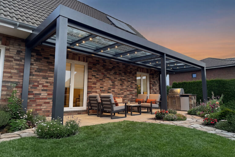 Moderne Aluminium-Terrassenüberdachung mit integrierter LED-Beleuchtung und Glasdach an einem Einfamilienhaus. Die überdachte Terrasse bietet einen stilvollen Outdoor-Wohnbereich mit Loungemöbeln und Außenküche für ganzjährigen Wetterschutz und höchsten Komfort im Garten.