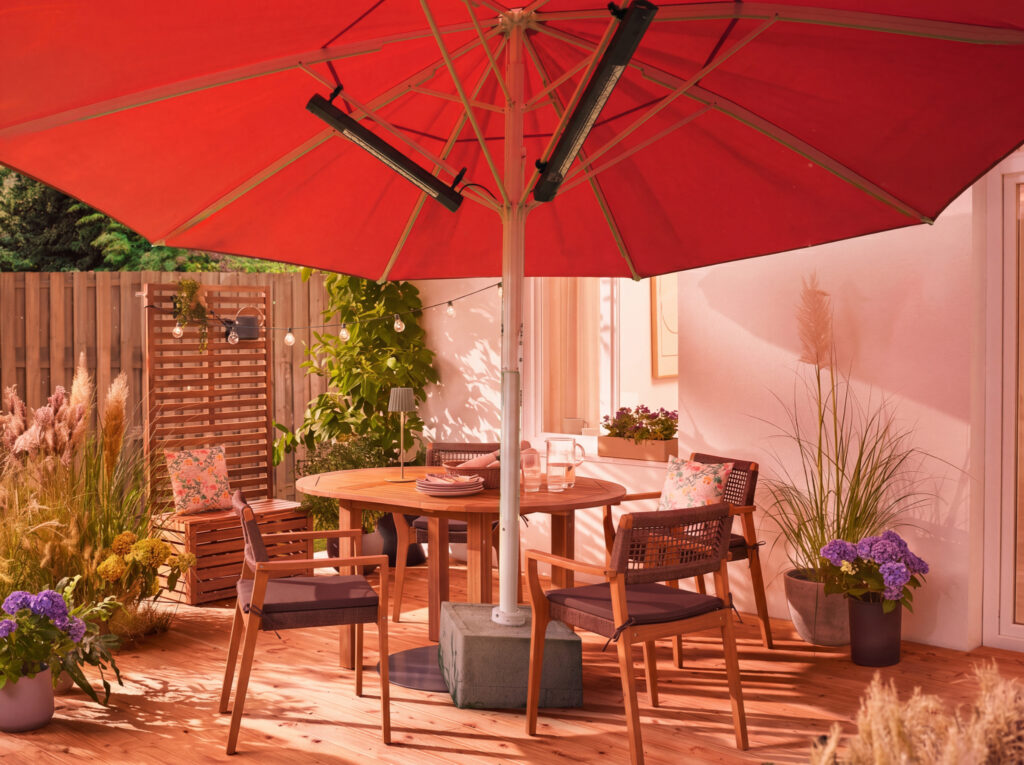 Großer roter Sonnenschirm mit integrierter Infrarotheizung über einer stilvollen Sitzgruppe auf einer modernen Holzterrasse im privaten Garten.